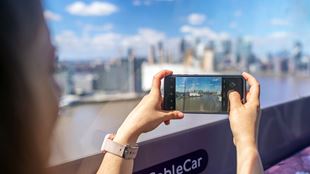 Someone holds a mobile phone taking a picture of the London skyline from the IFS Cloud Cable Car.