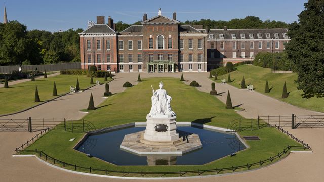 Statue de la reine Victoria dans les jardins de Kensington à Londres, avec le palais de Kensington en arrière-plan, par une journée ensoleillée.