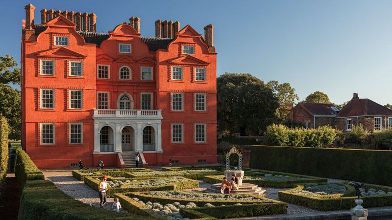 Admire Kew Palace, a former royal residence within the grounds of Kew Gardens. Image credit: visitlondon.com/Jon Reid. Image courtesy of Visit London/London & Partners. Kew Palace, a red brick royal residence, in the sunshine, with manicured hedges in front.