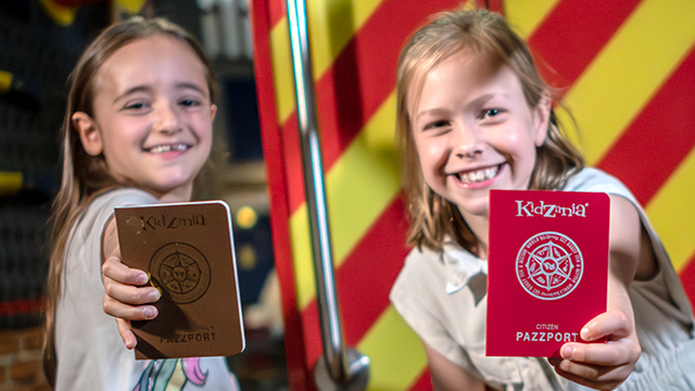 Emmenez vos enfants à KidZania, le seul endroit à Londres où vous pouvez vous essayer à différents métiers. visitlondon.com/Michael Barrow Deux enfants sourient à la caméra et montrent fièrement leur passeport KidZania.