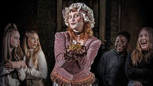 female actor stood in the middle, dressed in Victorian clothes holding a pie, with four people stood around her smiling and in shock