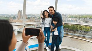 Visitors posing for a photo inside a London Eye capsule with the River Thames and Houses of Parliament visible through the glass.