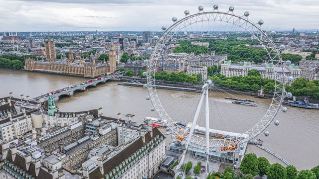 Wide view of the London Eye beside the River Thames, with the Houses of Parliament, Westminster Bridge and central London skyline.