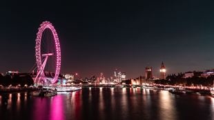 London Eye illuminated in pink at night, overlooking the River Thames with Westminster Bridge and the Houses of Parliament lit up.
