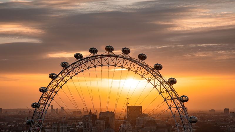 Soak up stunning sunset views as the London Eye rises above the city skyline. Image courtesy of Merlin. Upper section of the London Eye silhouetted against a golden sunset sky, with capsules visible along the wheel.