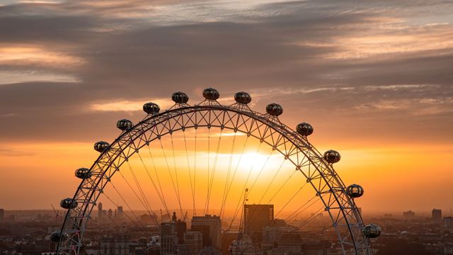 Upper section of the London Eye silhouetted against a golden sunset sky, with capsules visible along the wheel.