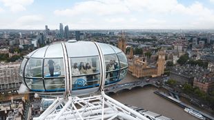 London Eye capsule with visitors inside, overlooking the river Thames, Westminster Bridge and the Houses of Parliament.