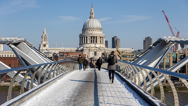 A view along Millennium Bridge towards St Paul's Cathedral, with snow and people walking on the bridge.