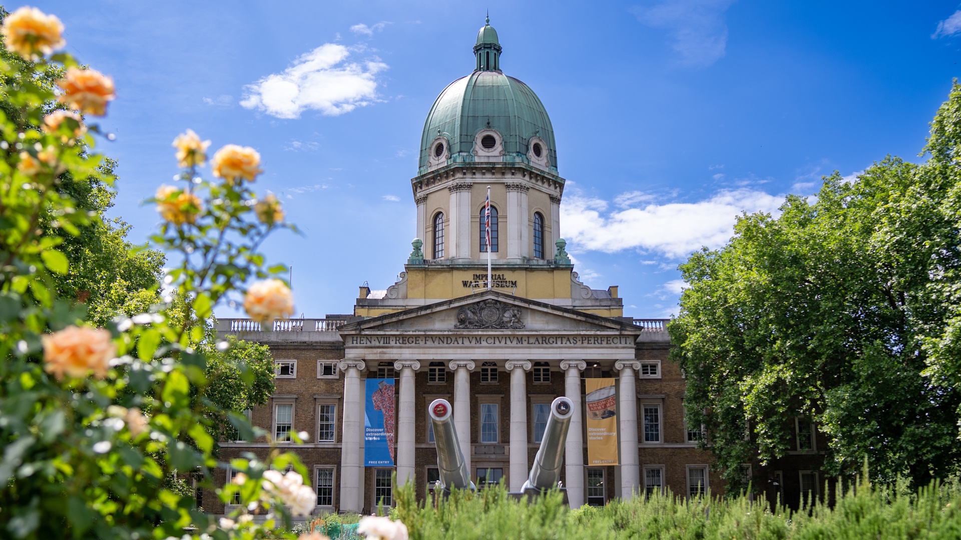 Explore wartime history at the Imperial War Museum. Image courtesy of Peter Cohen/London & Partners. Exterior view of London's Imperial War Museum with green dome and columns, on a sunny day with blue skies and yellow flowers and grass in the foreground.