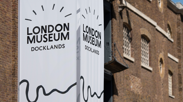 A large white sign with the London Museum Docklands logo stands in front of the museum building