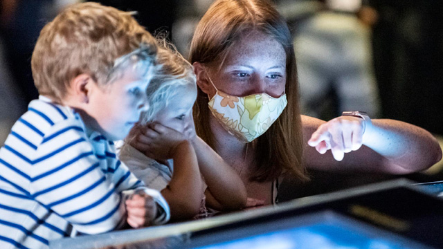 Une mère et ses deux enfants, un garçon et une fille, devant une exposition au Musée des sciences.
