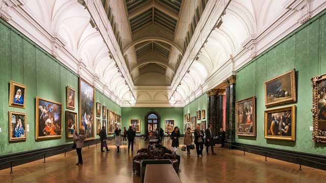 The interior of one of the rooms at The National Gallery, featuring green walls and numerous framed paintings.