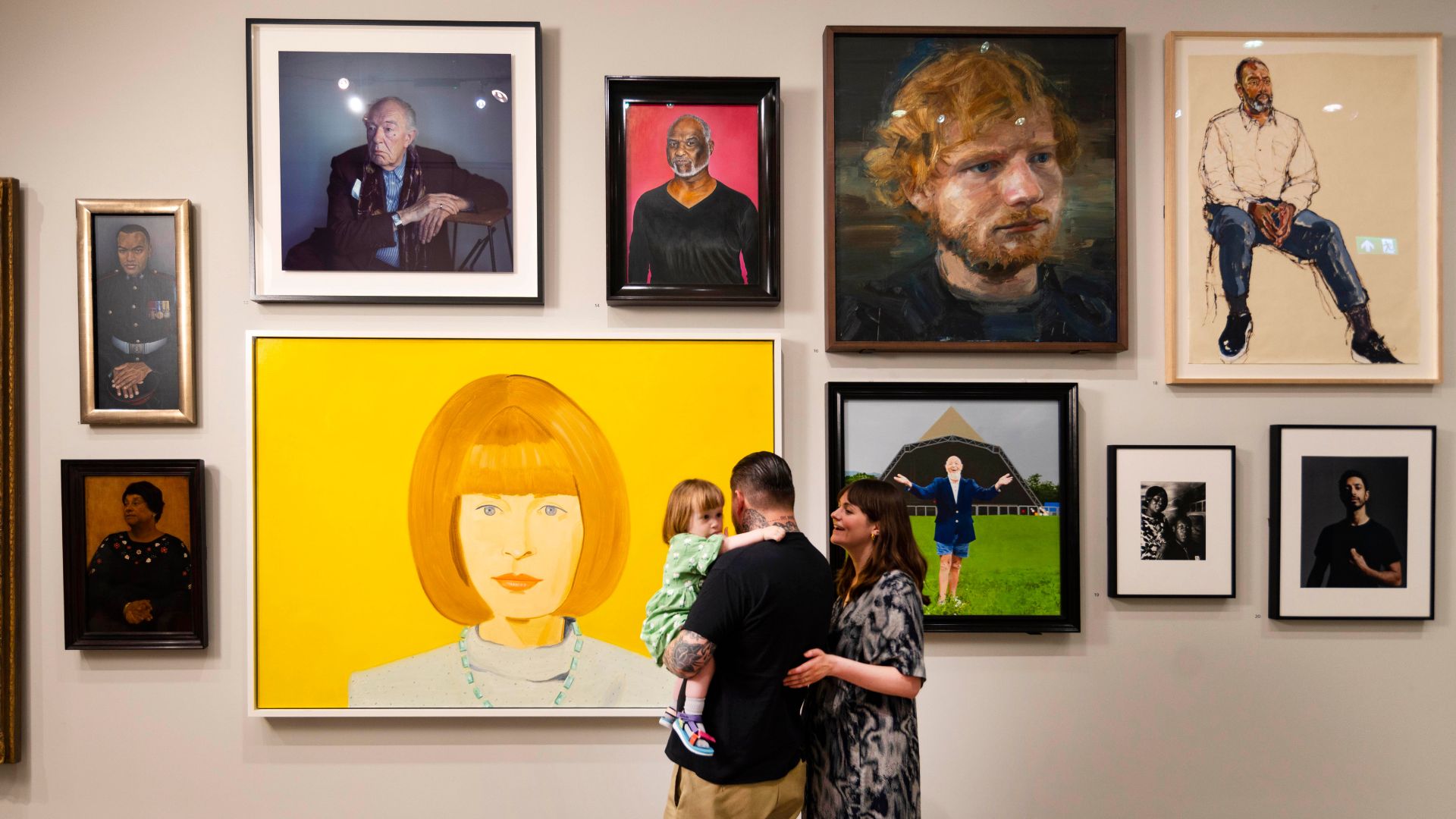 Several portraits of famous people on gallery wall with family looking at them.