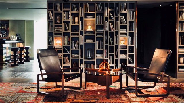 Two modern leather chairs next to a coffee table with a bookcase in the background and warm side lighting.