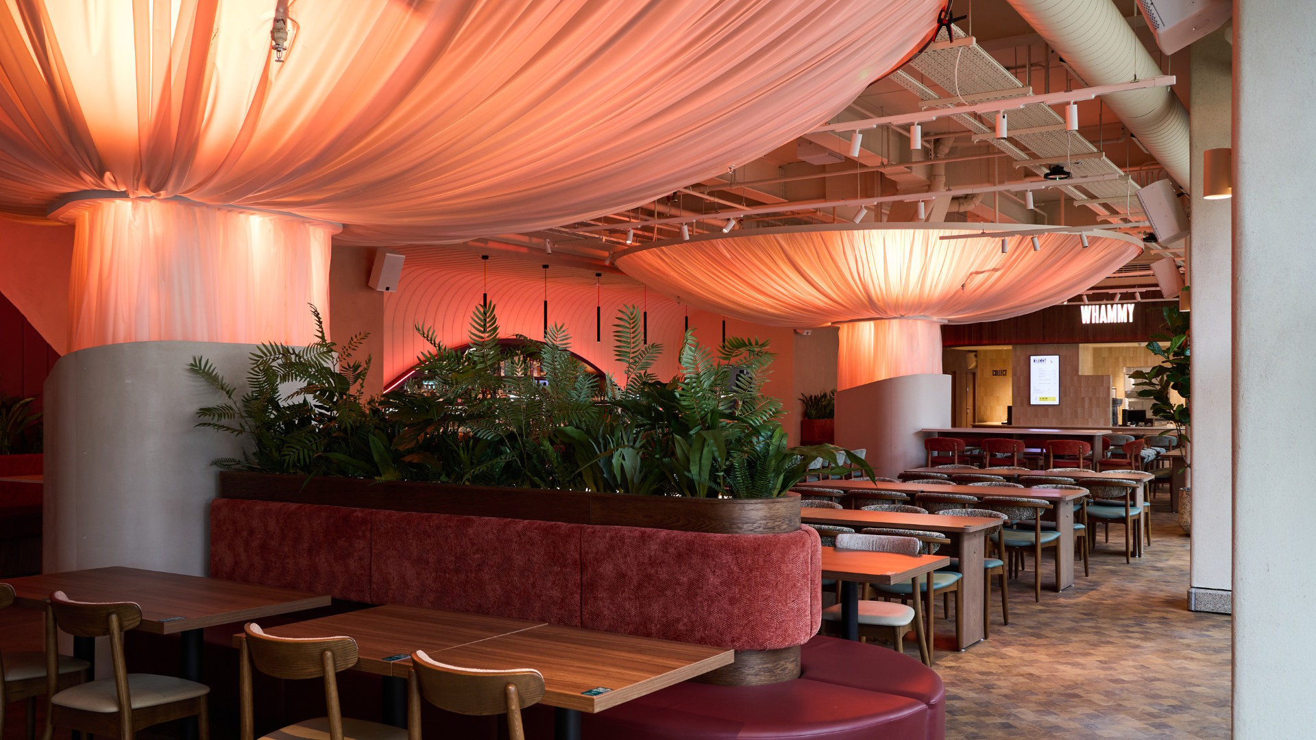 Dining tables and chais with plants and hanging lights inside an empty food hall.