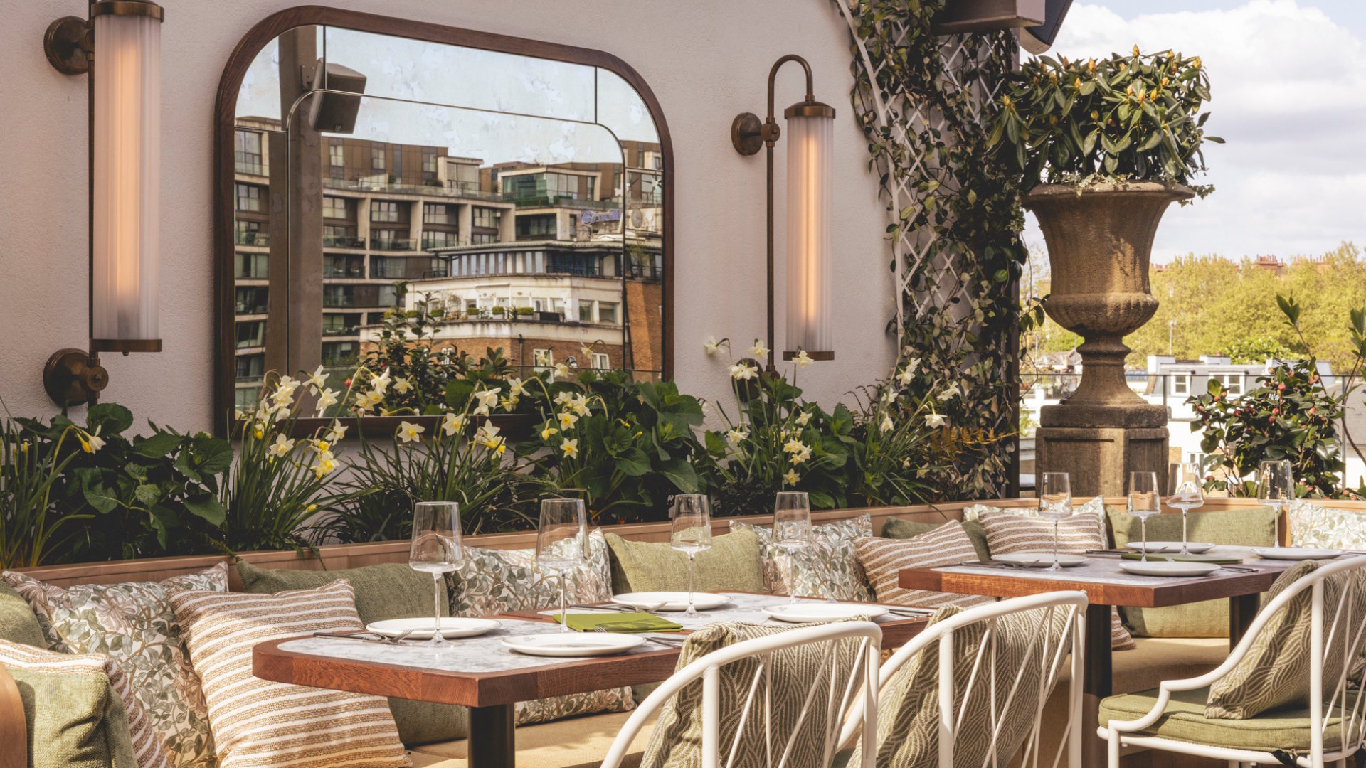 An elegant rooftop terrace inspired by the charm of an English garden with small tables and chairs, plants and hanging lights.