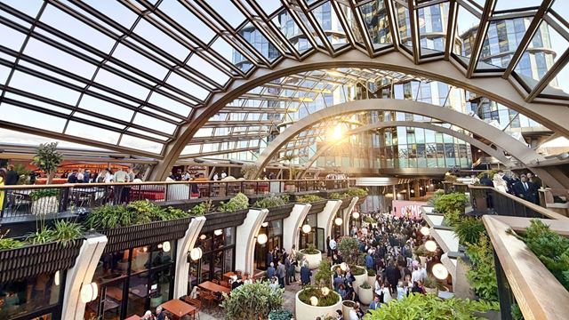 Visitors gather beneath Olympia’s striking glass canopy, surrounded by restaurants, greenery and the venue’s newly redeveloped public spaces.