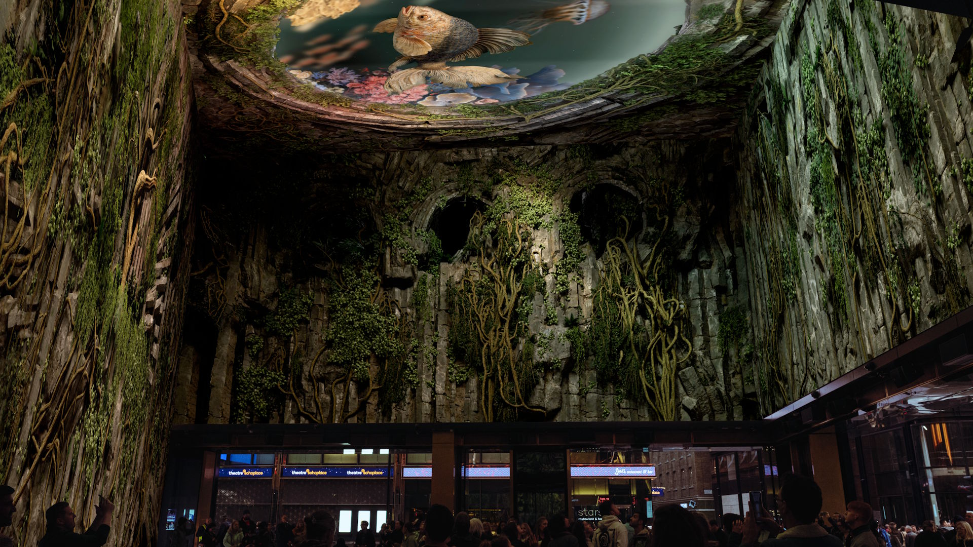 A display on Outernet's large wrap-around LED screens, showing green plants and vines tumbling down from the ceiling, where there's an image of a large fish.  