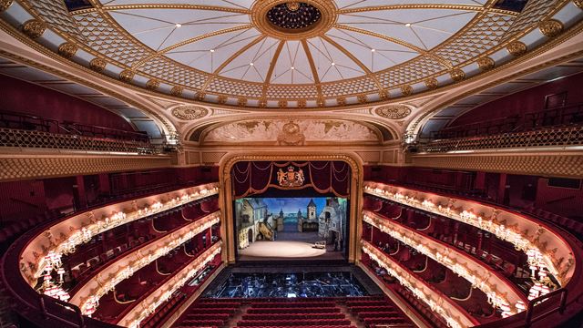A view of the Royal Opera House auditorium with its red velvet seats beneath a golden ceiling.