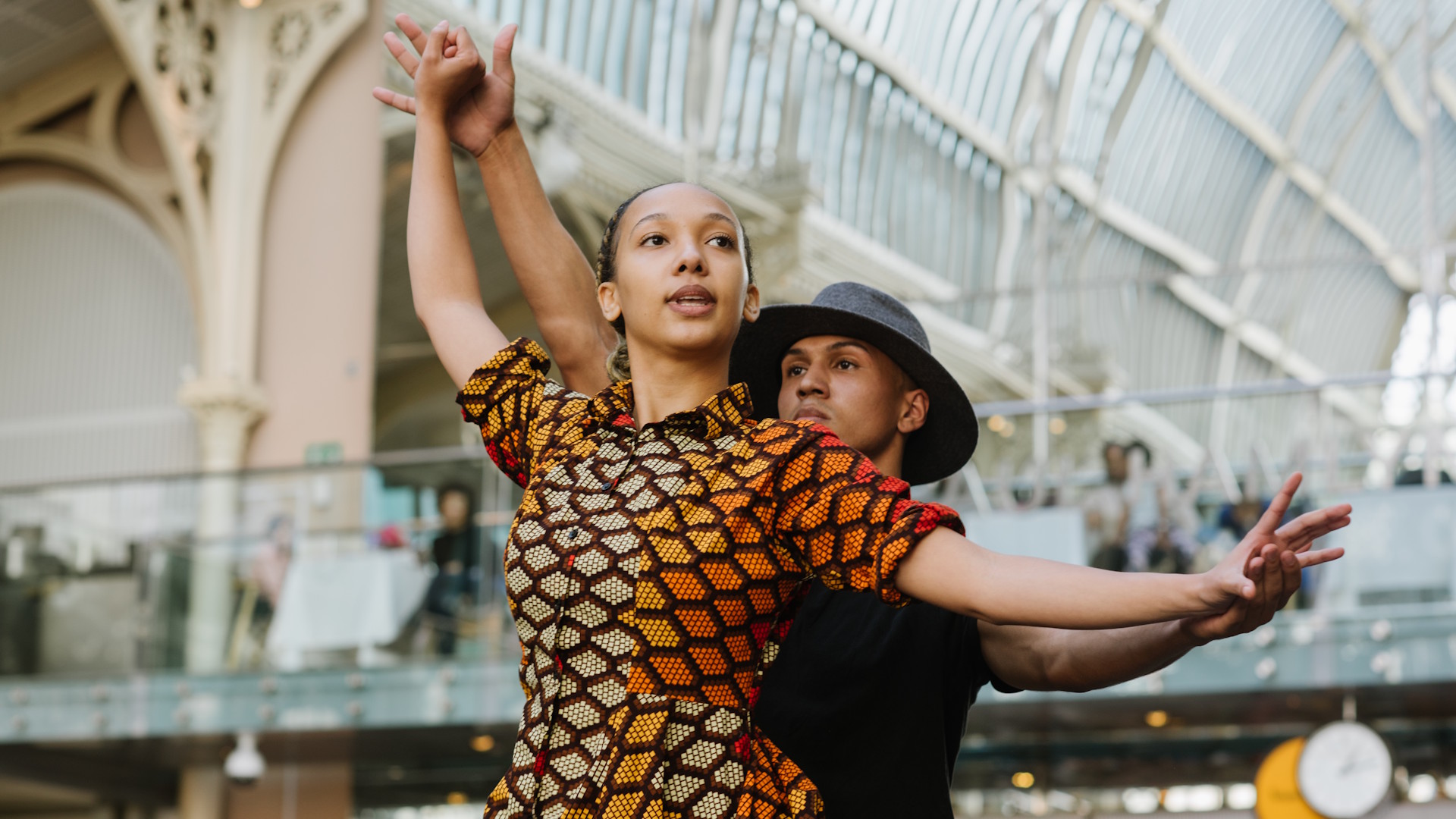 Two dancers perform in the Paul Hamlyn Hall at the Royal Opera House, with onlookers watching from the balcony.