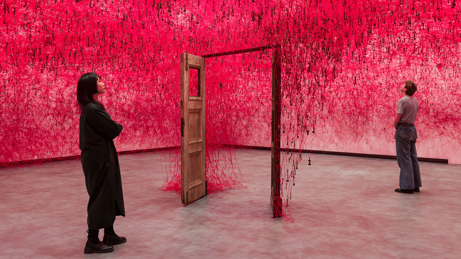 Two people looking at an art installation in front of a red background