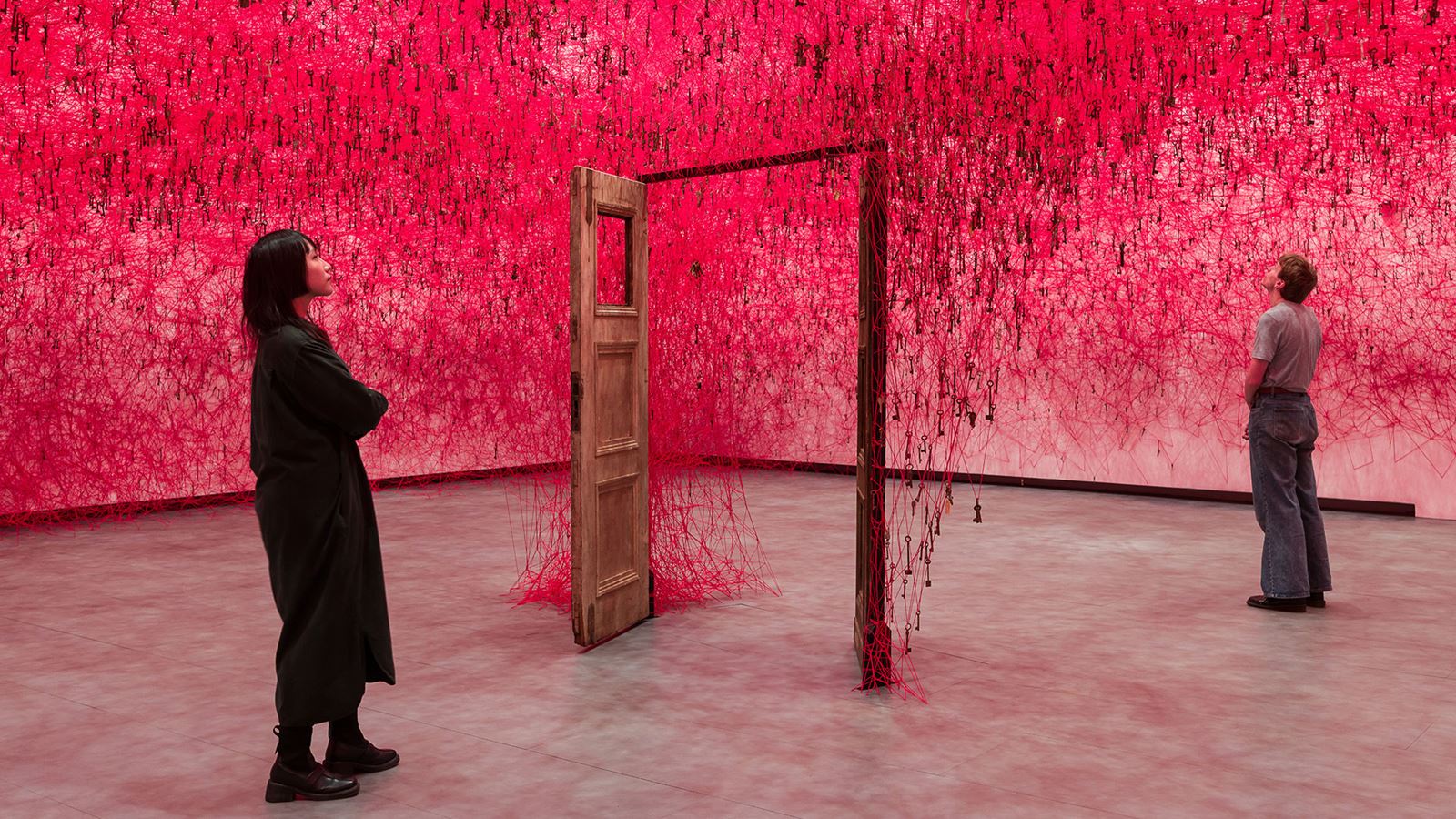Two people looking at an art installation in front of a red background