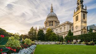  La cathédrale Saint-Paul par une journée radieuse, avec des nuages épars dans le ciel, une pelouse verte et un parterre de fleurs colorées au premier plan.