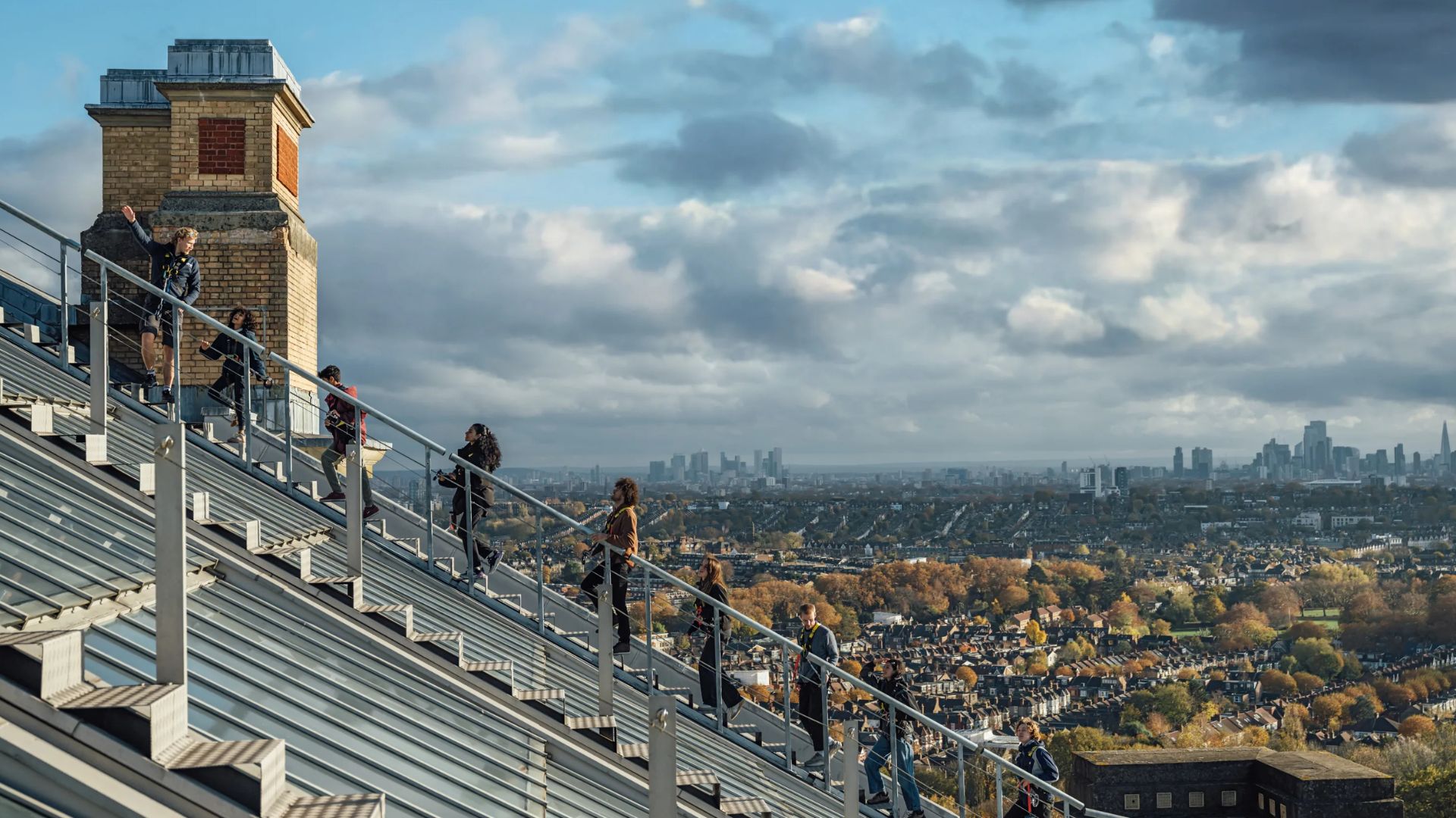 People climbing the rooftop steps of Alexandra Palace with panoramic views of London in the background.