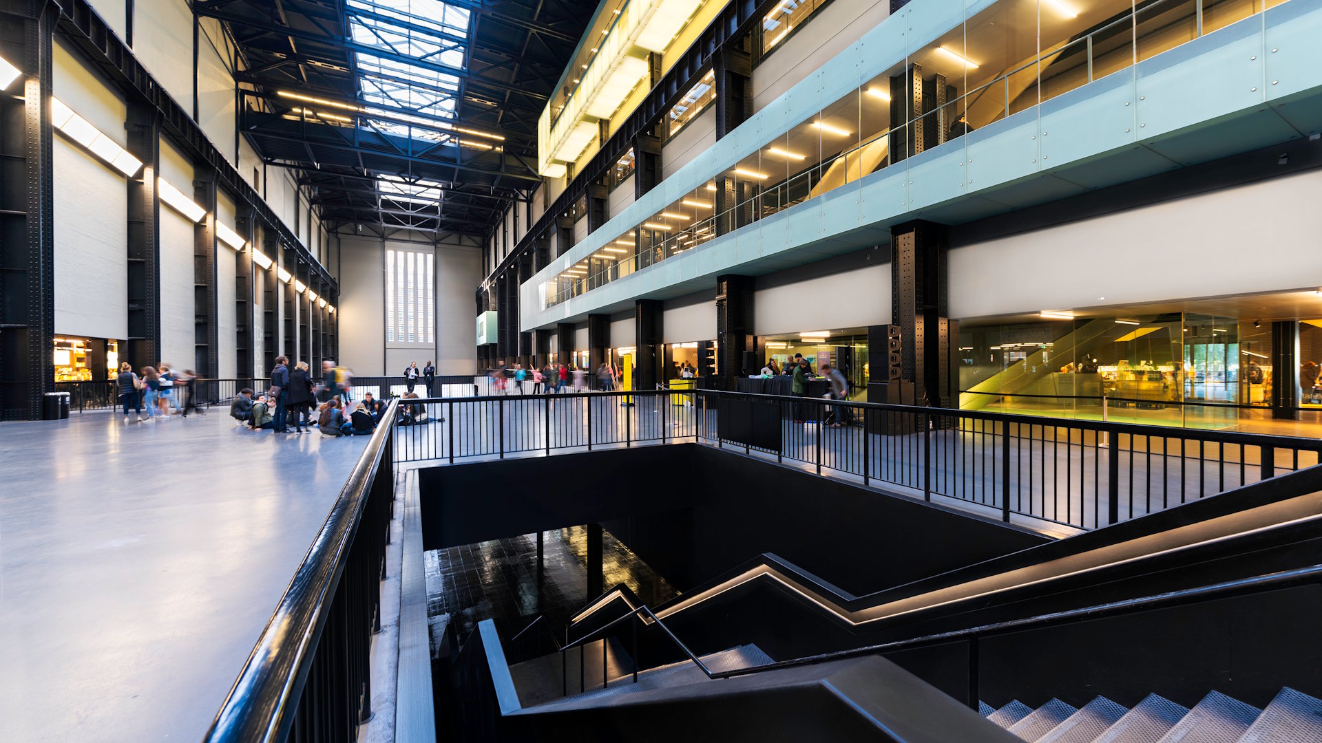 An interior view of the Turbine Hall at Tate Modern featuring a concourse and desks on the right.