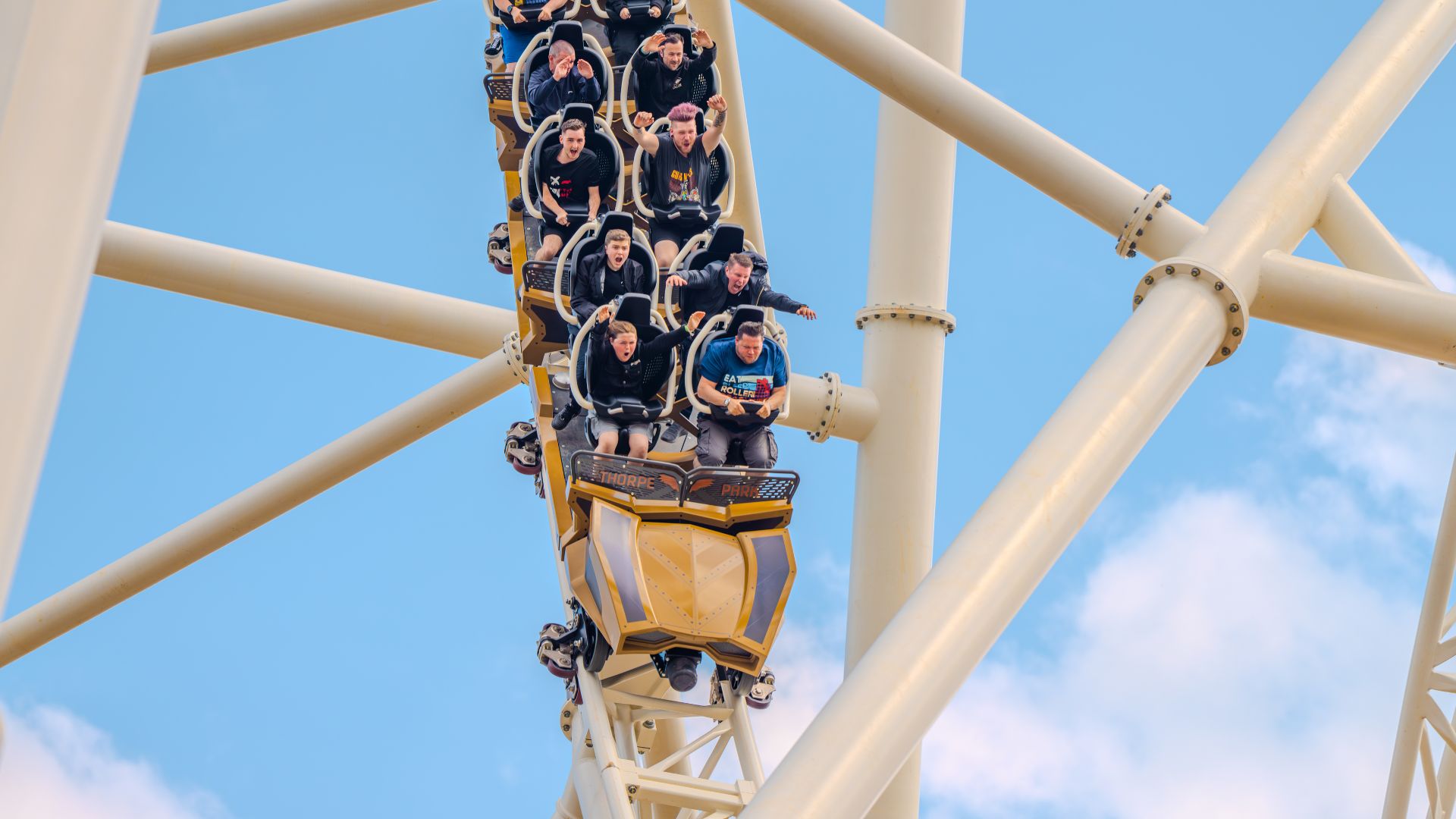 Riders seated on the Hyperia roller coaster at Thorpe Park as the train descends a steep drop against a blue sky.