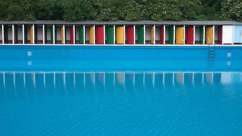 Enjoy a refreshing dip in Tooting Lido come rain or shine. Credit: Tooting Lido. Image courtesy of Tooting Lido. Looking across the pool at the colourful yellow, green and red doors of Tooting Bec Lido.