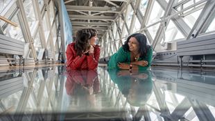 Deux femmes rient ensemble en regardant à travers la passerelle en verre du Tower Bridge. 