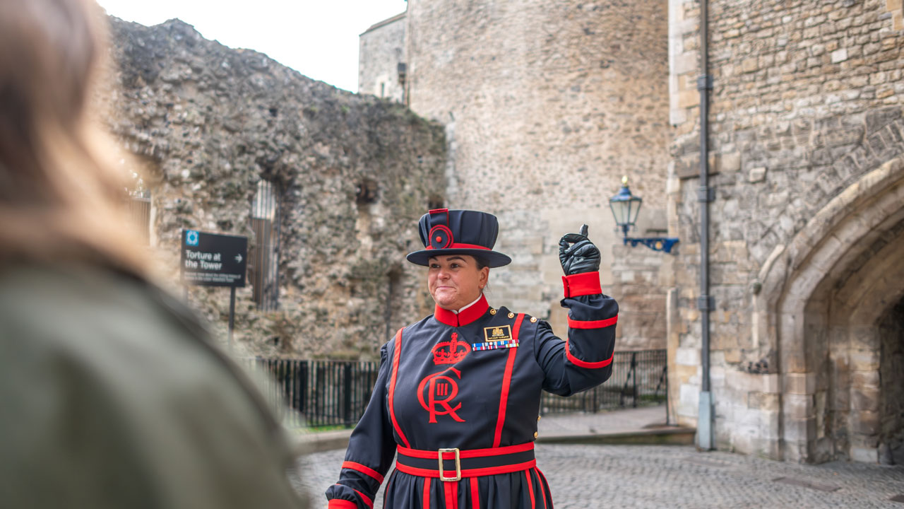 A female beefeater is leading a tour at the Tower of London.