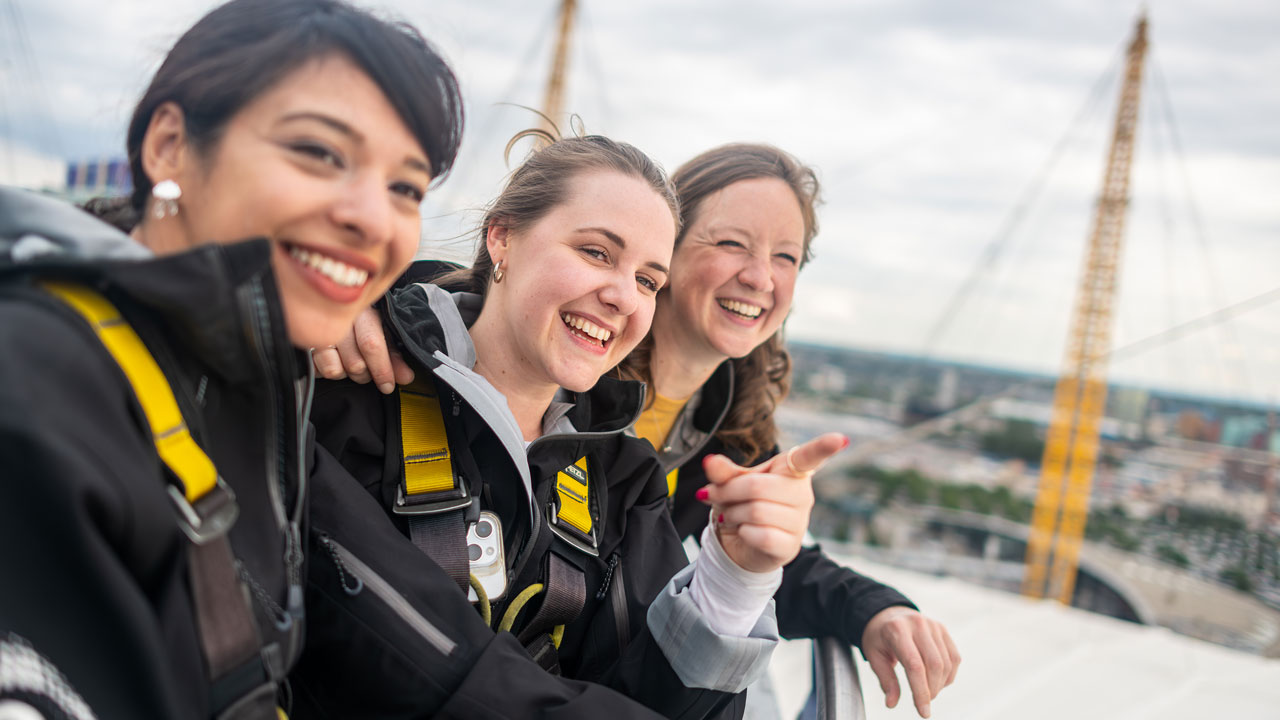 Préparez-vous pour un moment plein d'adrénaline avec Up at the O2 and profitez d'un panorama incroyable sur Greenwich. ©London & Partners/Michael Barrow Trois femme se trouvent sur le toit de l'O2 arena et observent le panorama sur Londres.