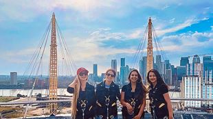 A group of women standing on the viewing platform Up at The O2, with the London skyline behind them on a sunny day