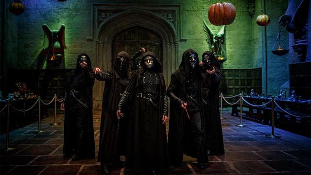 Five Death Eaters, dressed in long black robes and wearing silver masks, are standing in the Great Hall at Warner Bros. Studio Tour London – The Making of Harry Potter.