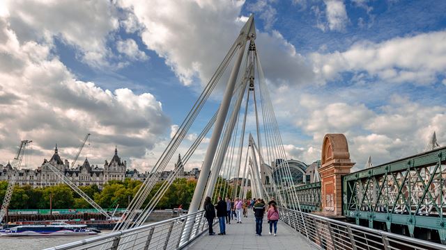 People walking across the Hungerford Bridge on a sunny day