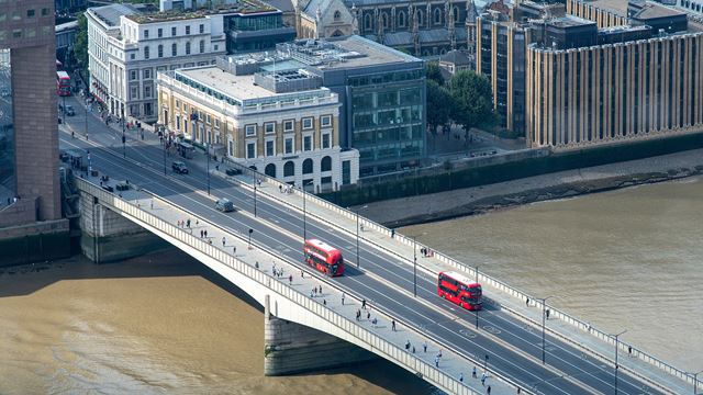 An aerial view of London Bridge with red buses going across it