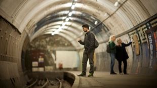 Two women in distance looking at vintage posters and man shining torch on tube tracks.