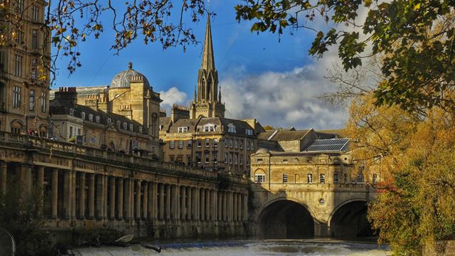 View of the Pulteney Bridge in Bath lit up by the sun against a blue sky. 