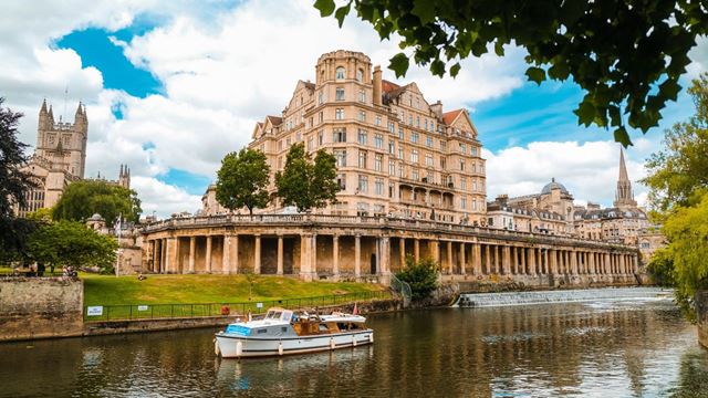 A white boat makes it way down the river Avon, passing Bath architecture. 