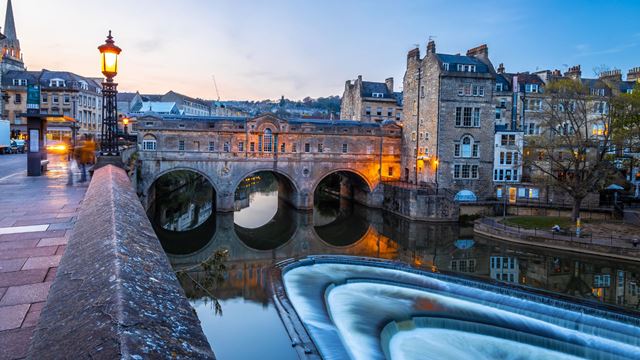 Pulteney Bridge in Bath illuminated at sunset with reflections on the River Avon.