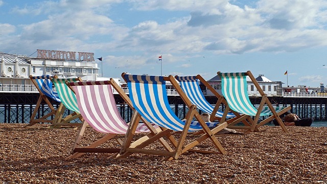 Low angle shot of pink, blue and green deckchairs on a pebbled beach, with Brighton Pier in the background