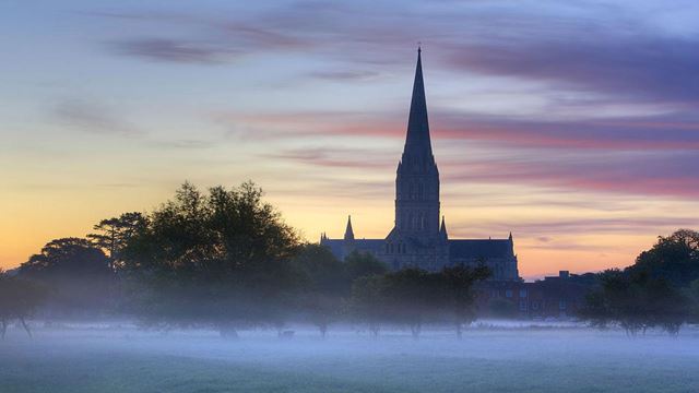 The Cathedral of Salisbury is surrounded by a white mist at sunrise.
