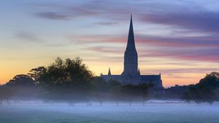 The Cathedral of Salisbury is surrounded by a white mist at sunrise.