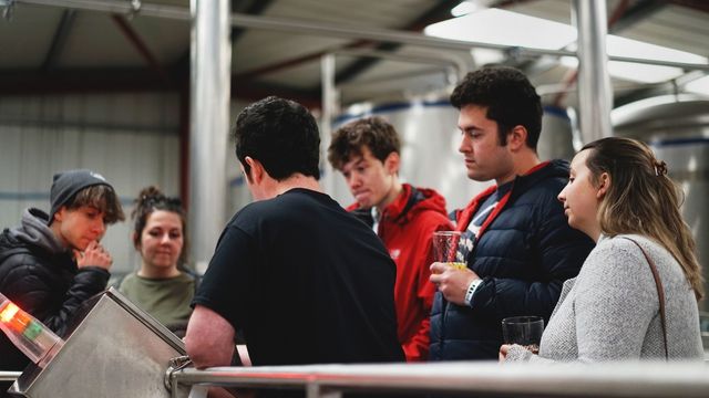 A  group of people stand together with a guide and try different beers in a york brewery,