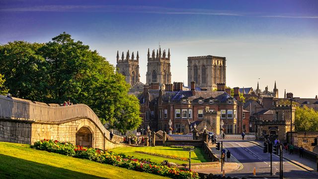 A bright blue sky above historic buildings in York including a majestic cathedral and people walking along a medieval wall.