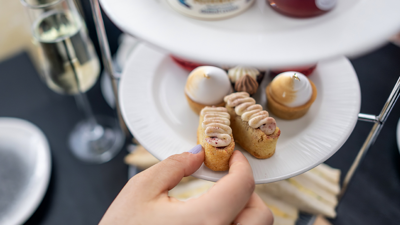 Savourez un éventail de sandwichs et de scones frais tout en admirant les célèbres monuments de Londres lors de la croisière "afternoon tea" de City Cruises. © London & Partners/Michael Barrow Quelqu'un choisit l'une des mini-pâtisseries présentées sur une assiette dans le cadre de l'afternoon tea servi servi à bord de la croisière City Cruises à Londres.