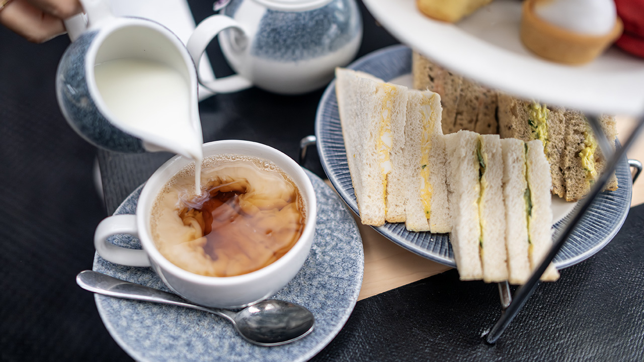 Savourez une délicieuse sélection de sandwichs et de gâteaux fraîchement préparés à bord de la croisière spéciale afternoon tea de City Cruises. © London & Partners/Michael Barrow Du lait est versé dans une tasse de thé noir pacée à côté d'une assiette contenant des finger sandwichs.
