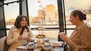 Two people sit at a table with an afternoon tea aboard a river thames cruise.